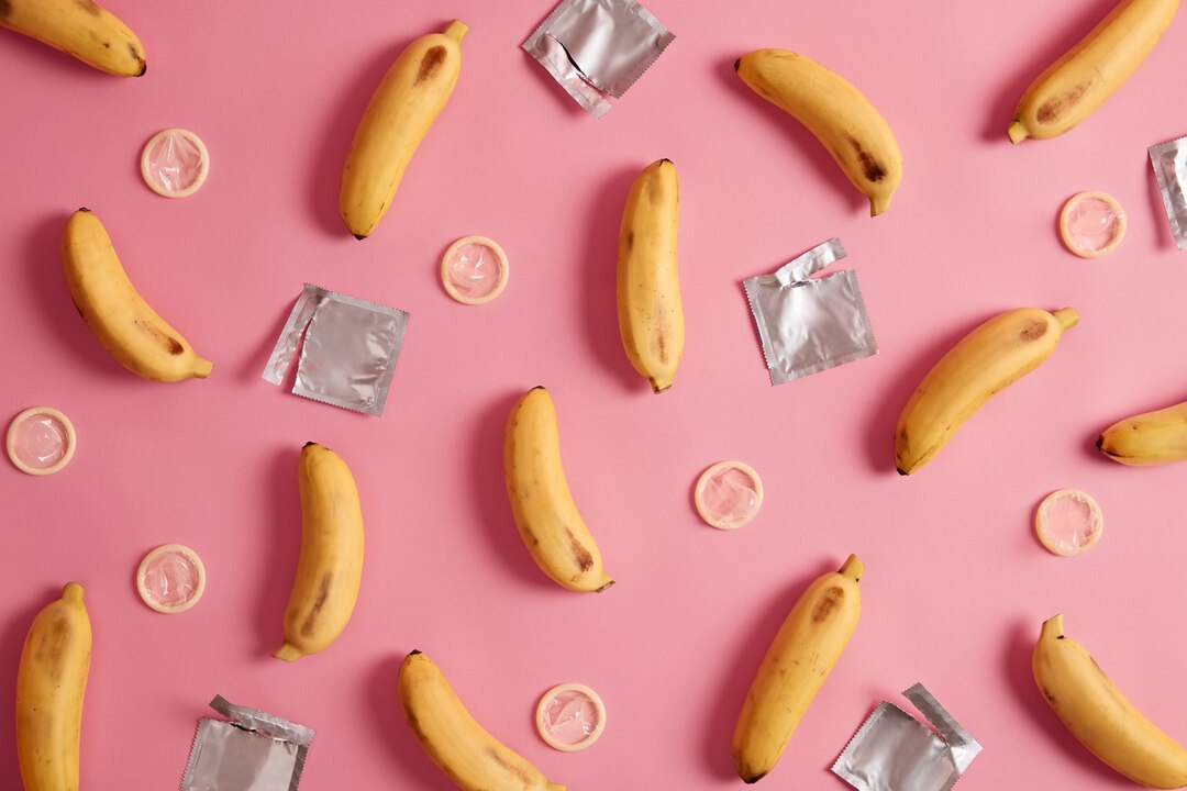 Multiple bananas surrounded by condoms against pink background